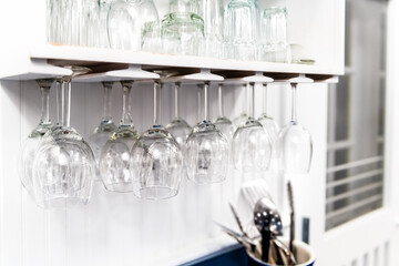 Closeup of modern kitchen interior design white shelf with upside down hanging empty wine glasses in room for storage of cups and nobody