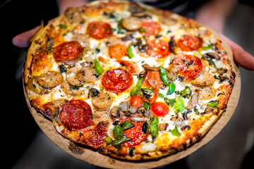 Small homemade or frozen pizza whole closeup macro hands holding with melted mozzarella cheese red...