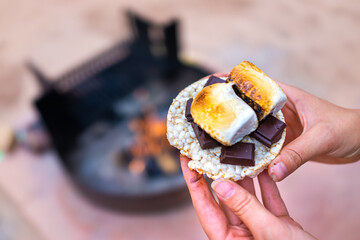 Young woman camping closeup hand holding roasted marshmallows smores with chocolate bar squares and...