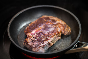 Closeup of brown charred crust on rare grass-fed ribeye rib eye meat steak cooking on non-stick frying pan grill with pepper salt seasoning