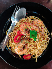 Delicious seafood Aglio Olio with big prawns on a black plate. Top view