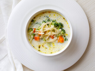 Healthy lunch colorful broccoli cheese soup in a bowl close-up on white table. Horizontal top view from above