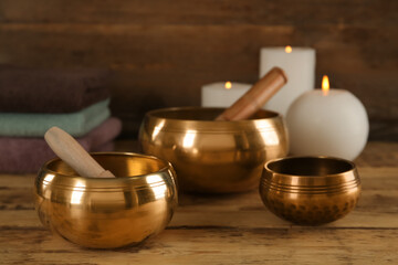 Golden singing bowls with mallets and burning candles on wooden table