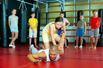 Young schoolgirl practicing basic self-defense moves during training at gym with male trainer