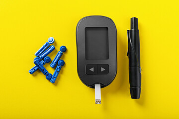 Digital glucometer with test strip, lancets and pen on yellow background, flat lay. Diabetes control