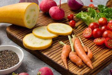 wooden board with fresh, eco, organic vegetables on gray background