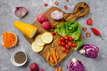 wooden board with fresh, eco, organic vegetables on gray background