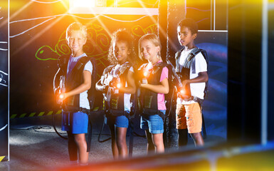 Portrait of multiracial group of smiling preteen kids with laser guns during lasertag game in dark room