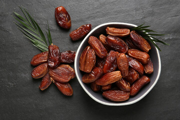 Tasty sweet dried dates and green leaves on black table, flat lay
