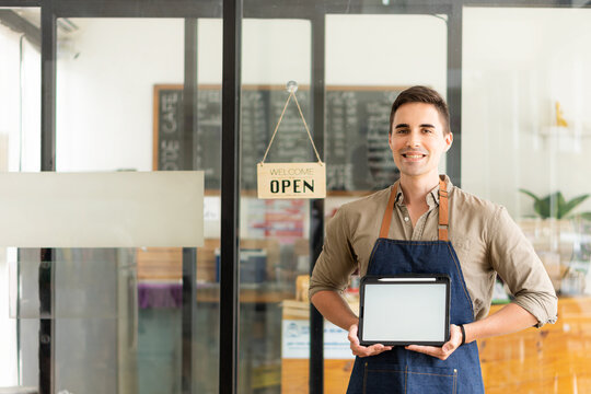 A young coffee shop owner with a white screen tablet stands in front of the shop smiling happily. food and beverage concept