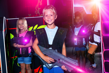 Smiling preteen boy standing with laser pistol in dark lasertag room during game with friends