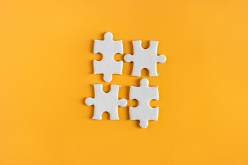 top view of unfinished or unattached four jigsaw puzzle pieces on yellow or orange background....