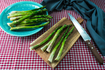 Group of green asparagus spears on a wooden cutting board on a table with a checkered tablecloth.