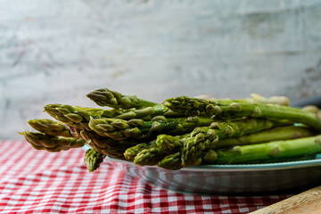 Group of raw green asparagus on a vintage plate on a table with a checkered tablecloth.