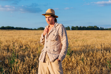 Tall handsome man dressed in a coarse linen suit and hat standing at golden oat field