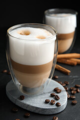 Delicious latte macchiato, cinnamon sticks and coffee beans on black table