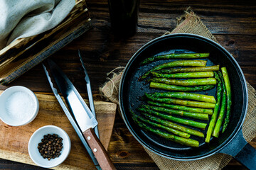 Preparation of green asparagus cooked in butter in a pan on a wooden counter.