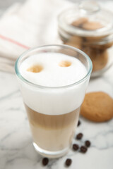 Delicious latte macchiato, cookies and coffee beans on white marble table