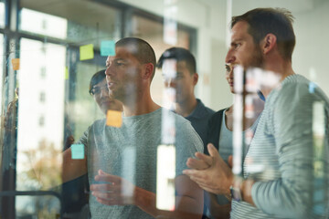 Planning is the first step. Cropped shot of a group of young designers planning on a glass board.