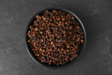 Bowl of aromatic dry cloves on black table, top view