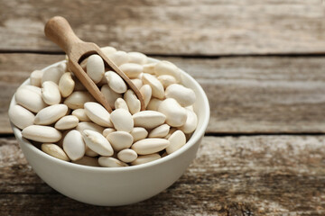 Bowl and scoop with uncooked white beans on wooden table, space for text