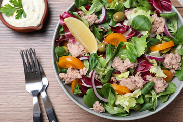 Bowl of delicious salad with canned tuna and vegetables served on wooden table, flat lay