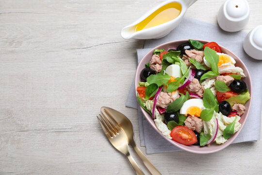Bowl of delicious salad with canned tuna and vegetables served on white wooden table, flat lay. Space for text