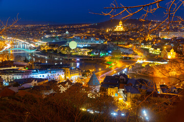 Night spring cityscape of historical area of Tbilisi illuminated by colorful lights with view of modern bow-shaped bridge across Mtkvari River, Georgia