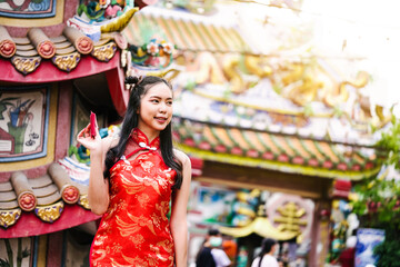Asian girl wearing a cheongsam is feeling happy. holding a red red envelope in front of the shrine.