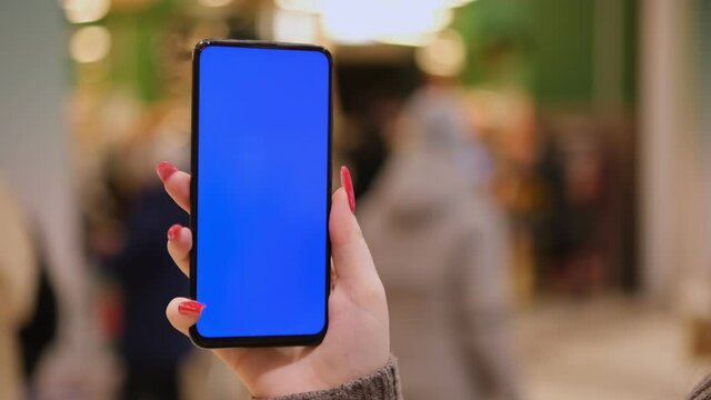 young woman holding a phone with chroma key on the background of a supermarket. The girl is holding a smartphone with a green screen and in the mall. Business woman working on smartphone surfing the