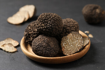 Black truffles in wooden plate on grey table, closeup