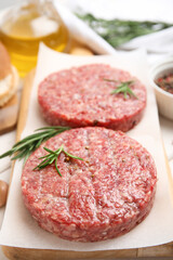 Raw hamburger patties with rosemary on wooden board, closeup
