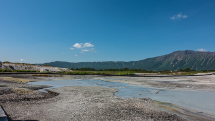 The caldera of an extinct volcano has rocky soil with sulfur deposits. The water in the hot springs is translucent. Tourist wooden paths have been laid. Mountains against the blue sky. Kamchatka. Uzon