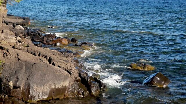Close up of white waves rolling in from the blue water of Lake Superior onto the rocky shoreline in Minnesota. Clip with zoom in on shore of Gitchi-Gami.