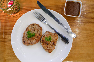 Pork steak in white plate on wooden table.