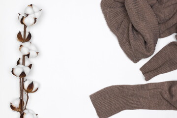 Warm brown wool sweater with white cotton flower sprig on white background top view. Cozy winter wear. Copy space