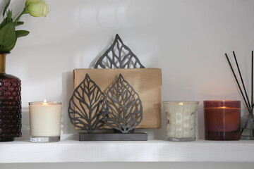 Burning candles. flowers and decor on white shelf