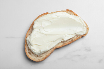Slice of bread with tasty cream cheese on white marble table, top view