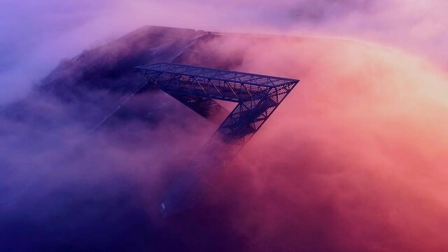 Monument on mountain in early morning light with sun shining from one side and clouds passing over the top, drone shot