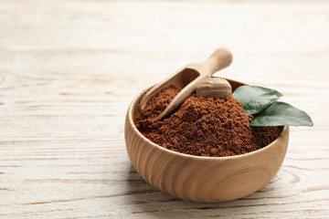 Nutmeg powder and seed with green leaves in bowl on white wooden table, space for text