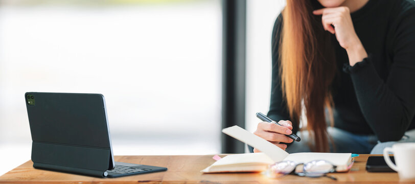 Cropped image of young businesswoman sitting at desk office, thinking and planning abult private business investment, using digital tablet. Business strategy and investment concept.