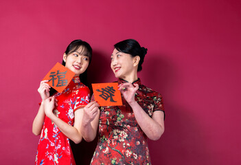 Asian mother and daughter in traditional cheongsam with copy space isolated on red background.The...