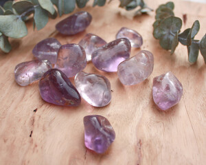 Amethyst crystal tumbled stone, smooth purple rock on wood with leaves. 