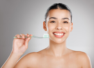 Call it insurance for your teeth. Studio shot of an attractive young woman brushing her teeth against a grey background.