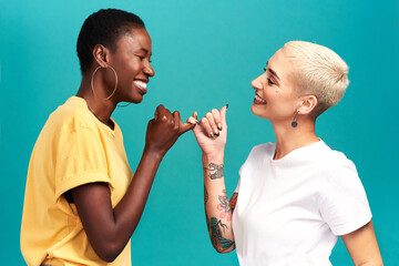You can count on me. Studio shot of two young women linking their fingers against a turquoise...