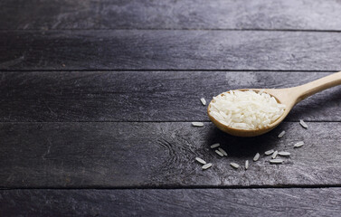 Close up Thai jasmine uncooked rice grain on wooden spoon on black table
