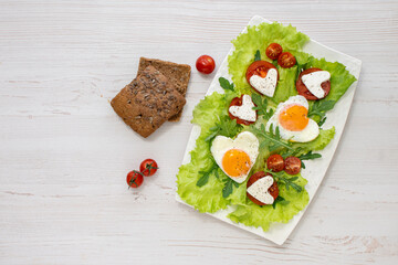 Breakfast on Valentine's Day. A plate of heart-shaped scrambled eggs, tomatoes, cheese and herbs and grain bread. View from above. Space for text. Diet breakfast.