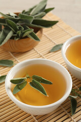 Cup of aromatic sage tea with fresh leaves on table