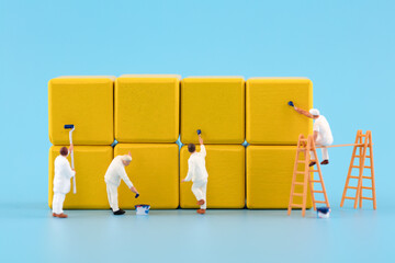 Miniature creative workers are painting building blocks