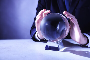 Businessman using crystal ball to predict future at table, closeup. Space for text